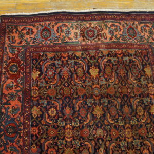 Traditional navy and red patterned rug featuring a wide peach border sits on rustic wood planks.