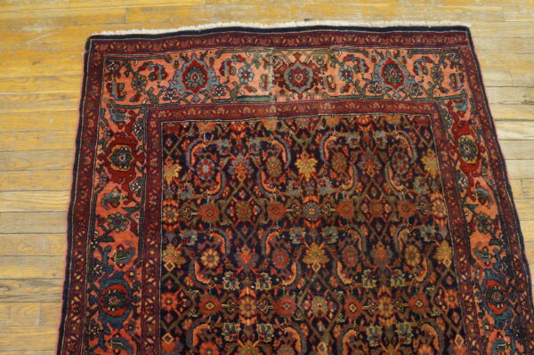 Traditional navy and red patterned rug featuring a wide peach border sits on rustic wood planks.