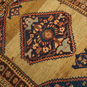 Close-up of a rug featuring a tan and brown field with a navy blue and orange geometric medallion.