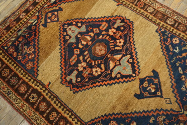 Close-up of a rug featuring a tan and brown field with a navy blue and orange geometric medallion.