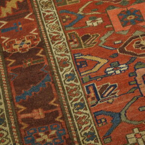 Detailed view of a rust red geometric rug, bordered by tan, resting on light wooden floorboards.