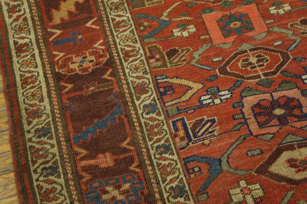 Detailed view of a rust red geometric rug, bordered by tan, resting on light wooden floorboards.