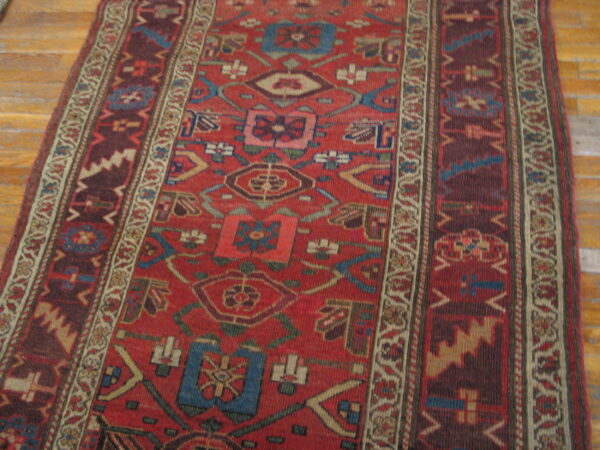 Geometric red runner with stylized blue, beige, and brown patterns displayed on light wood flooring.