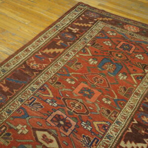 Detailed red, brown, and blue geometric rug with multiple borders rests on light wooden plank flooring.