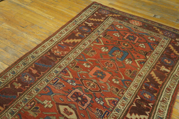 Detailed red, brown, and blue geometric rug with multiple borders rests on light wooden plank flooring.