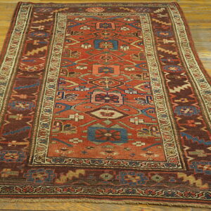 Low-pile runner rug featuring an intricate geometric pattern in rust, blue, and dark brown on light wood planks.