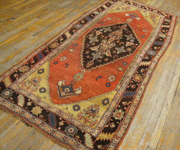 Traditional rust and dark brown medallion rug featuring gold spandrels rests on worn wood flooring.