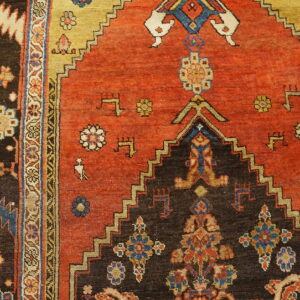 Geometric rug detail showing a rusty red field, dark stepped medallion, and stylized motifs on wooden flooring.