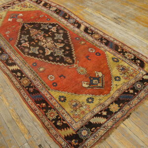 Red and gold patterned rug featuring a dark central medallion on faded wooden floorboards.