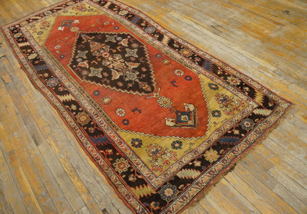Red and gold patterned rug featuring a dark central medallion on faded wooden floorboards.