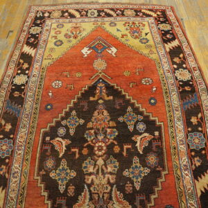 Low pile rug with a stepped brown and orange geometric pattern and complex borders on wood planks.