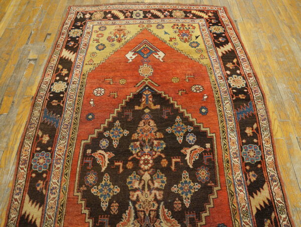 Low pile rug with a stepped brown and orange geometric pattern and complex borders on wood planks.