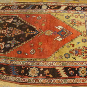 Rust and brown tribal rug with a stepped medallion and geometric floral borders on light wooden flooring.