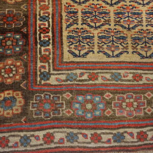 Detailed view of a rug corner with a beige field, brown border, and geometric floral patterns in red and blue.