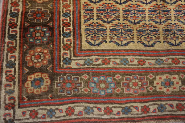 Detailed view of a rug corner with a beige field, brown border, and geometric floral patterns in red and blue.