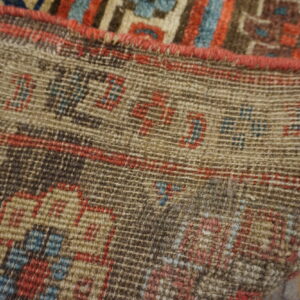 Detailed view of a rug's tightly woven backing showing red and blue knotted geometric patterns.