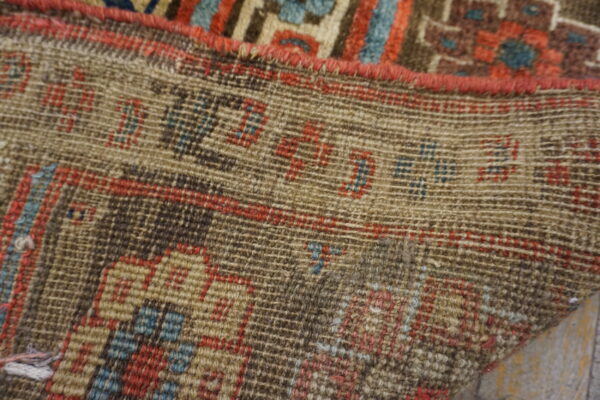 Detailed view of a rug's tightly woven backing showing red and blue knotted geometric patterns.