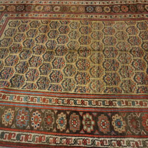 Distressed traditional rug with gold and multicolored field, laid upon light gray wood flooring.