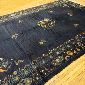 A large, deep navy rug with gold and light blue floral motifs is displayed on light wooden flooring.