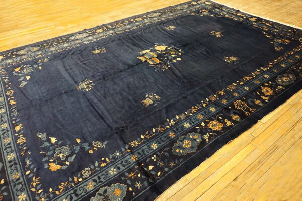 A large, deep navy rug with gold and light blue floral motifs is displayed on light wooden flooring.
