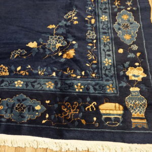 Plush navy rug detail showing a border of golden and teal floral designs and vases on wood flooring.
