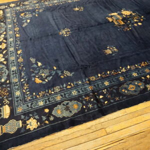 Navy blue rug featuring gold and teal floral designs and a visible sheen, resting on aged wood flooring.