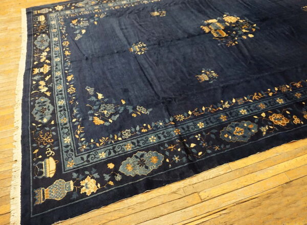 Navy blue rug featuring gold and teal floral designs and a visible sheen, resting on aged wood flooring.