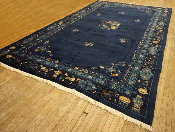 Navy area rug featuring floral and vase motifs in gold and teal, laid on plank wood flooring.