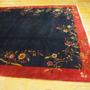 Navy rug with a wide red border and multicolor floral design lying on light wooden flooring.
