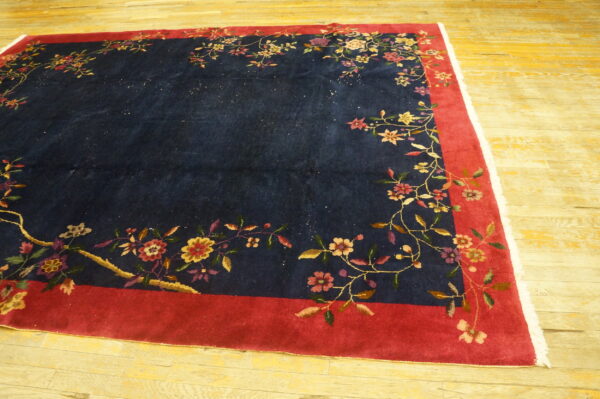 Navy rug with a wide red border and multicolor floral design lying on light wooden flooring.