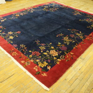High-pile navy rug with red border and multi-colored floral vines lies on yellow hardwood floors.