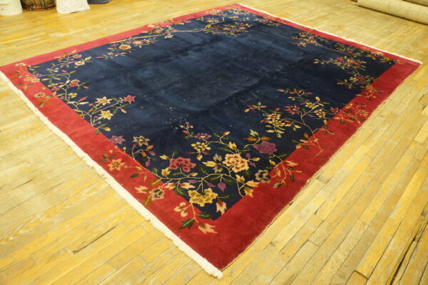 High-pile navy rug with red border and multi-colored floral vines lies on yellow hardwood floors.