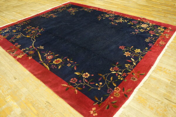 Navy blue rug with colorful floral vines along a red border resting on light wood plank flooring.