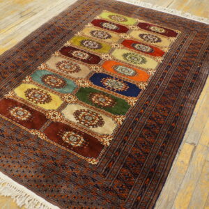 Colorful rectangular rug featuring medallion boxes and dark geometric borders rests on distressed blonde wood flooring.