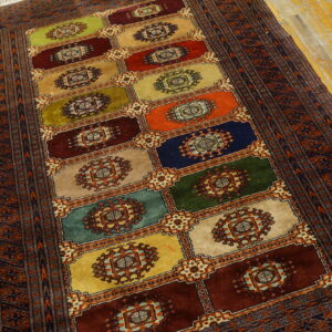Multicolor block rug with central medallions and a patterned border rests on distressed wood flooring.