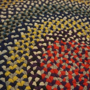 Braided rug featuring thick rings of multicolored coils in red, yellow, blue, purple, and gray.