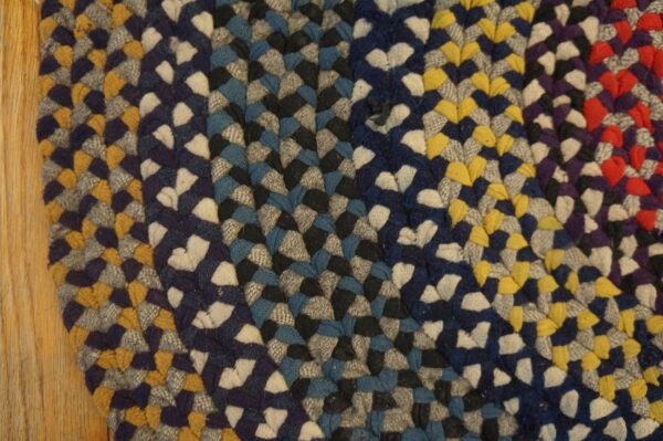 Thick braided rug with colorful sections of blue, gray, yellow, red, and white resting on wood floor.