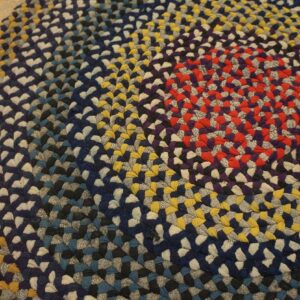 Close-up of a circular braided rug in rings of red, navy, gray, and gold on hardwood.