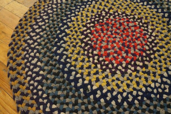 Close-up of a circular braided rug in rings of red, navy, gray, and gold on hardwood.