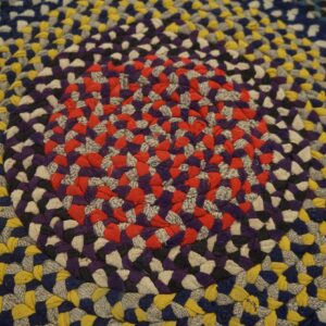 Close-up of a multicolored braided round rug featuring concentric rings of red, purple, yellow, and blue.