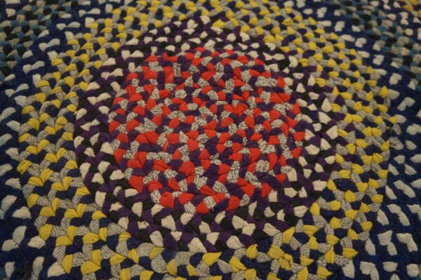 Close-up of a multicolored braided round rug featuring concentric rings of red, purple, yellow, and blue.