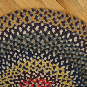 Rounded, braided rug in blue, yellow, gray, and red colors rests on light wooden floorboards.