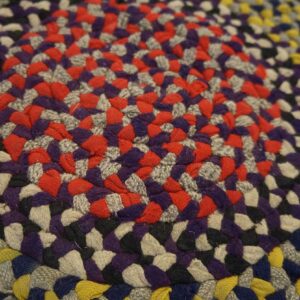 Braided rug macro view featuring concentric rings of red, purple, gray, yellow, black, and blue colors.