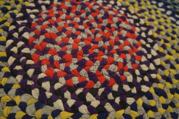 Braided rug macro view featuring concentric rings of red, purple, gray, yellow, black, and blue colors.