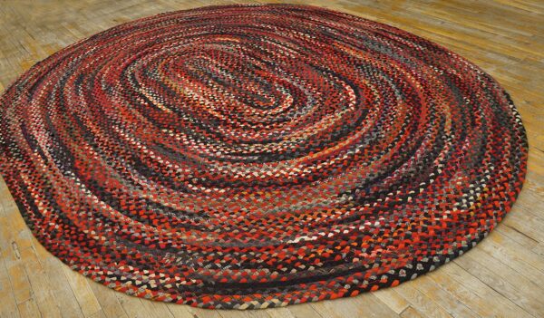 Multicolor braided round rug with red and black tones on light, distressed wood flooring.