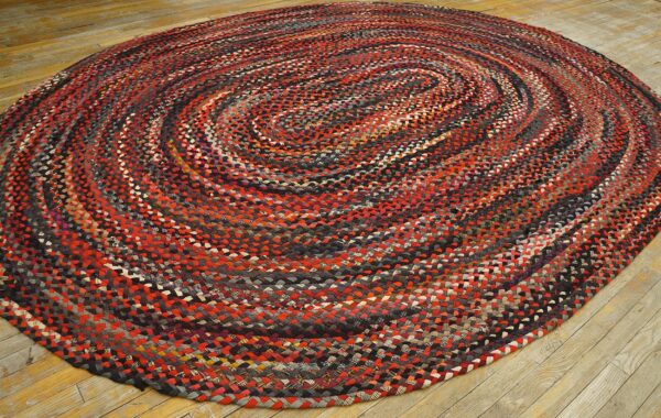 Oval braided rug with concentric red, gray, and black spirals covers light wood flooring.
