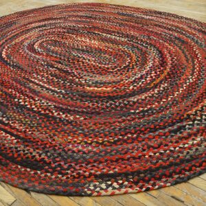 Multicolored braided round rug with red and black swirls on light wood flooring.