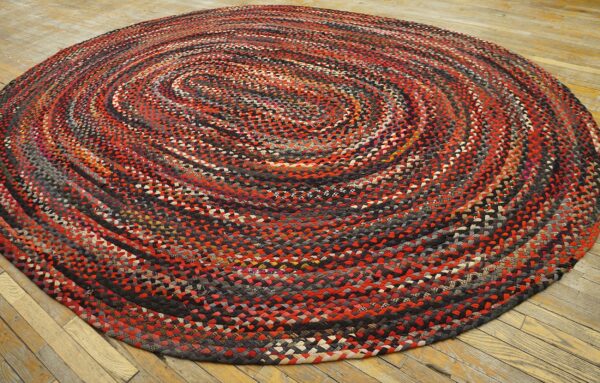 Multicolored braided round rug with red and black swirls on light wood flooring.