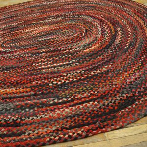 Round braided rug in variegated red, black, gray, and cream, resting on distressed wood floors.