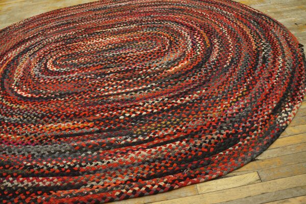 Round braided rug in variegated red, black, gray, and cream, resting on distressed wood floors.